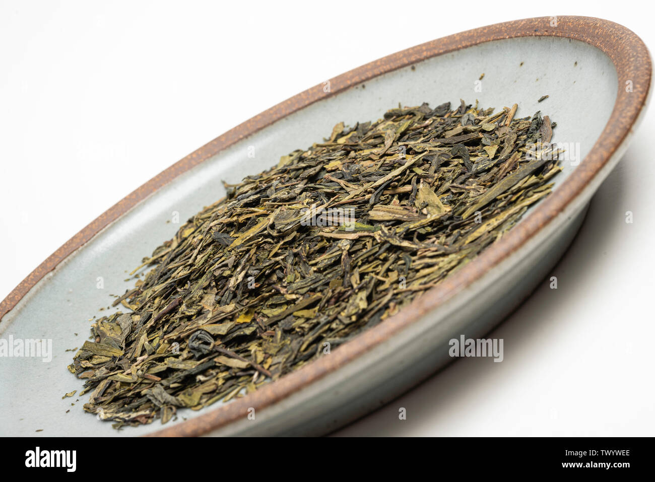 Un prodotto di studio shot di un mazzetto di cinesi secchi di foglie di tè verde sul round emerald porcellanato impostato su sfondo bianco. Foto Stock