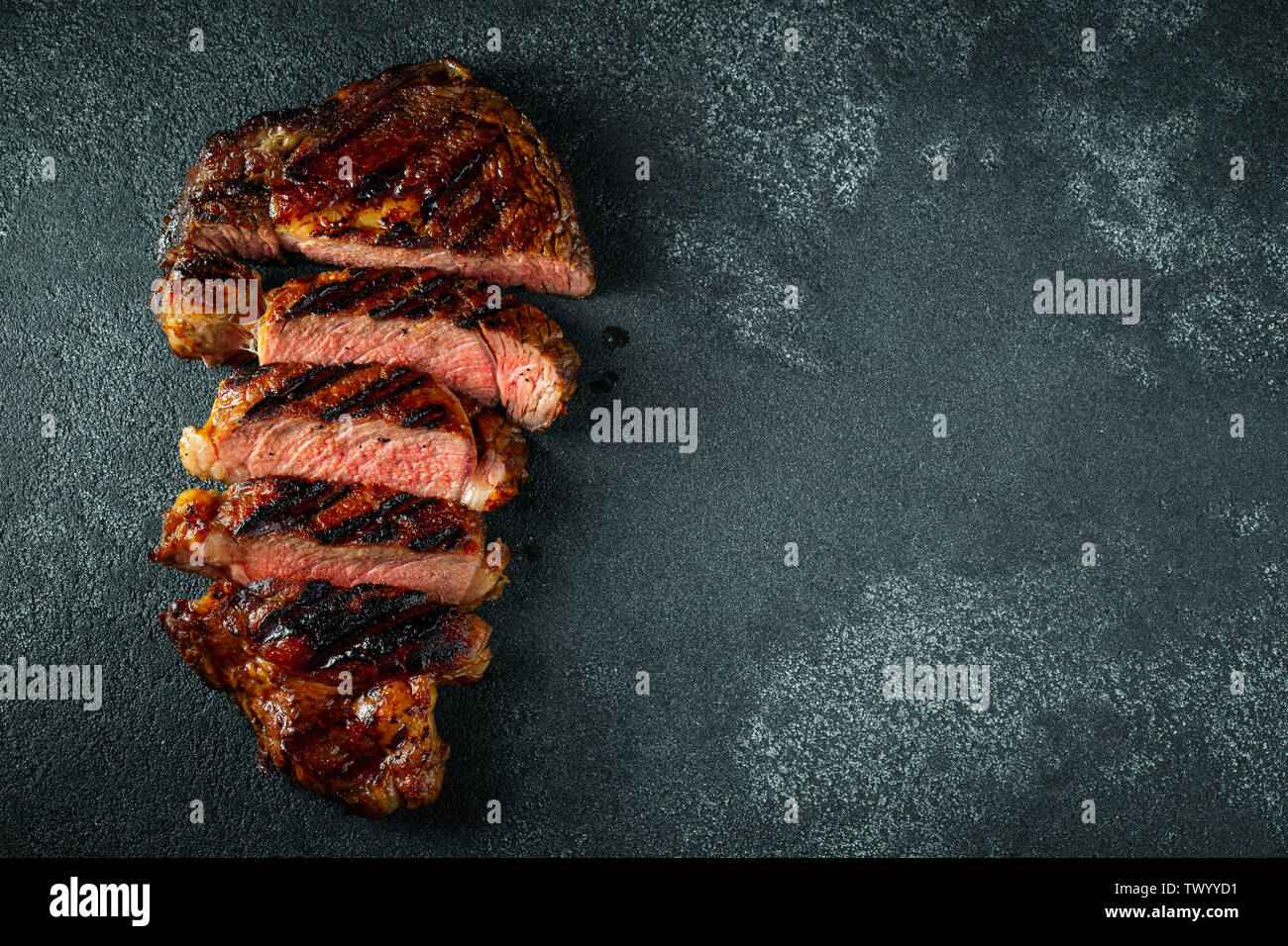 Tagliata, bistecca alla griglia con pepe, aglio, sale e timo su una pietra scura sullo sfondo. Vista da sopra con copia spazio. Lay piatto Foto Stock