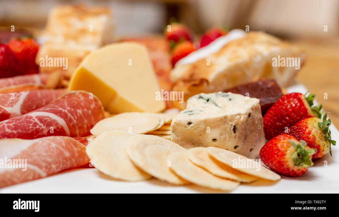 Fino vicino immagine di un piatto di antipasti con una miscela di carni fredde, fragole, crackers, formaggio e pane, con una profondità di campo ridotta Foto Stock