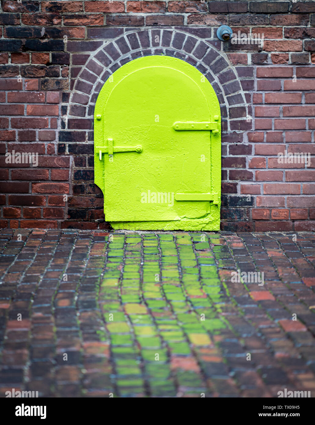 La pioggia riflette una piccola verde porta in acciaio in mattoni della Distillery District, Toronto, Ontario, Canada. Foto Stock