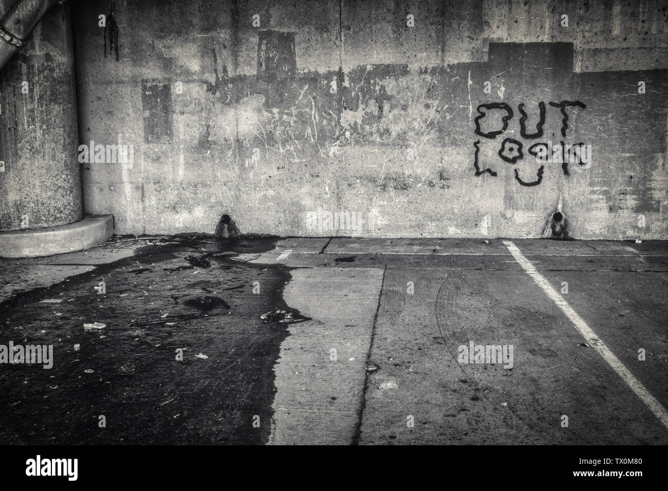 Le parole "Look Out' dipinta come graffiti su una parete di una schifezza, con una chiazza di petrolio sul terreno Foto Stock
