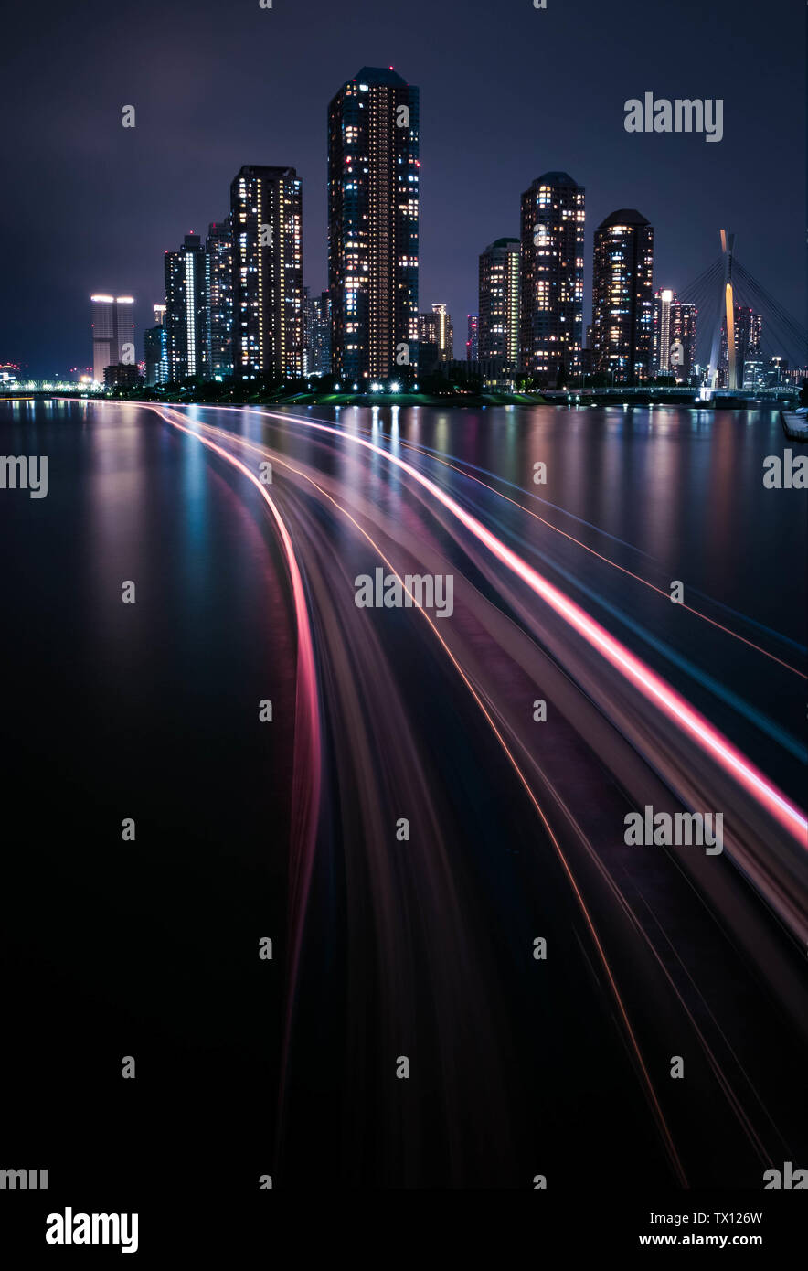 Vista notturna del condominio di lusso a Tokyo accanto al fiume con un sentiero di luce dalla barca. Foto Stock