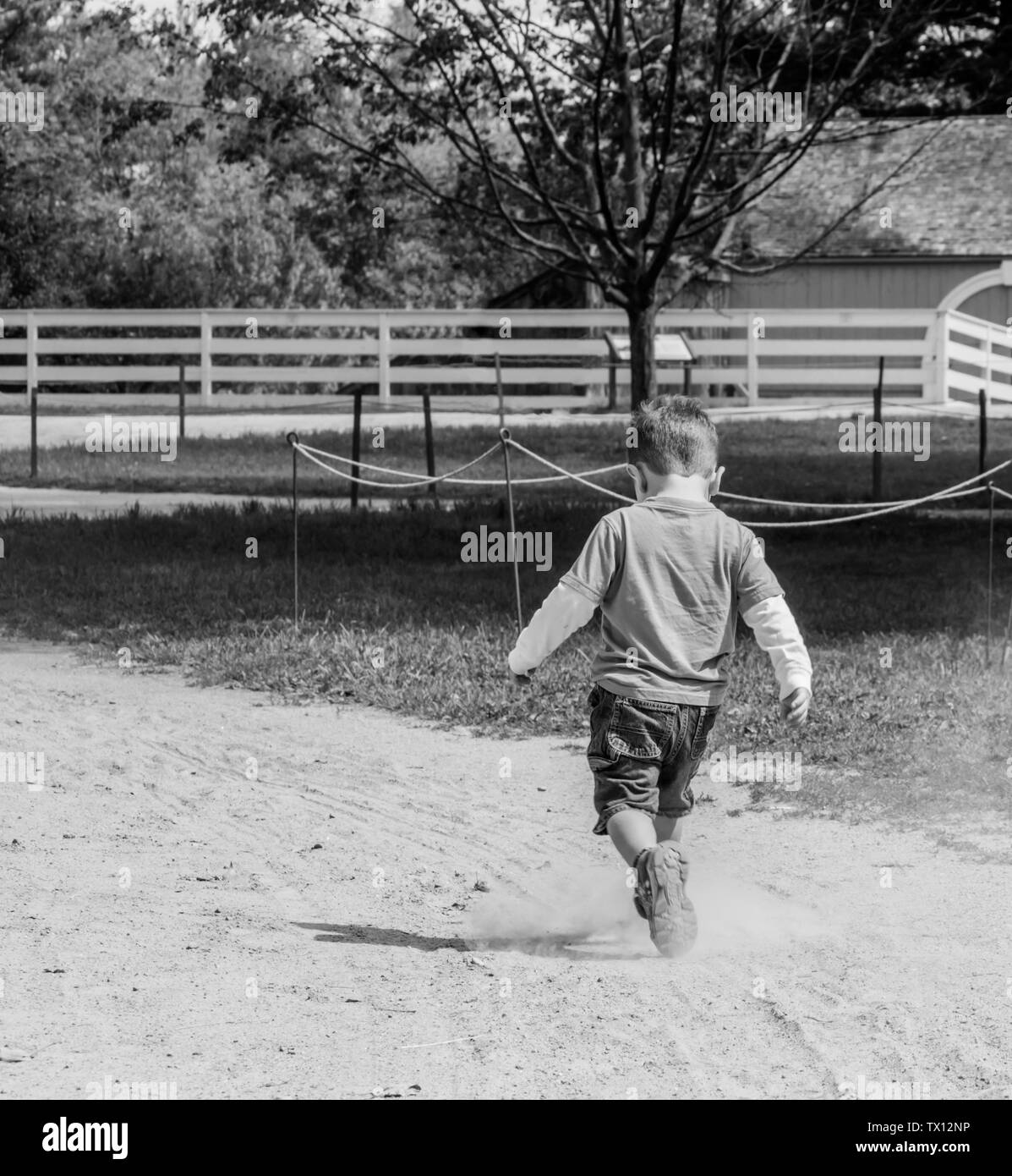 Ragazzo che corre in una strada fangosa a un colpo di fattoria in bianco e nero Foto Stock