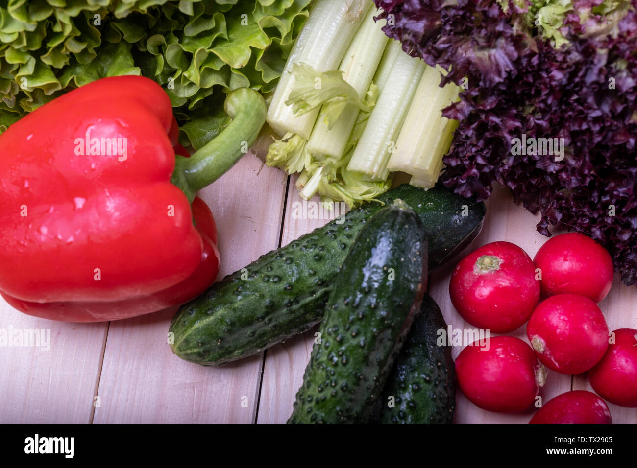 Le verdure su una luce tavolo in legno, la paprica rossa, sedano, lattuga, cetrioli e ravanelli Foto Stock