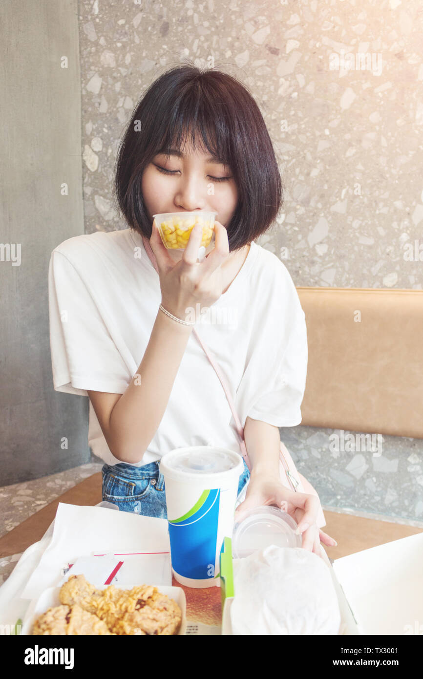 Una ragazza felice di mangiare una tazza di mais in un ristorante. Foto Stock