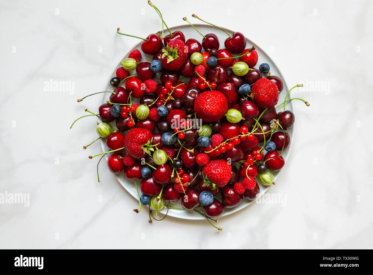 Varie estate freschi frutti di bosco in una piastra su marmo bianco tavola. Vista superiore Foto Stock