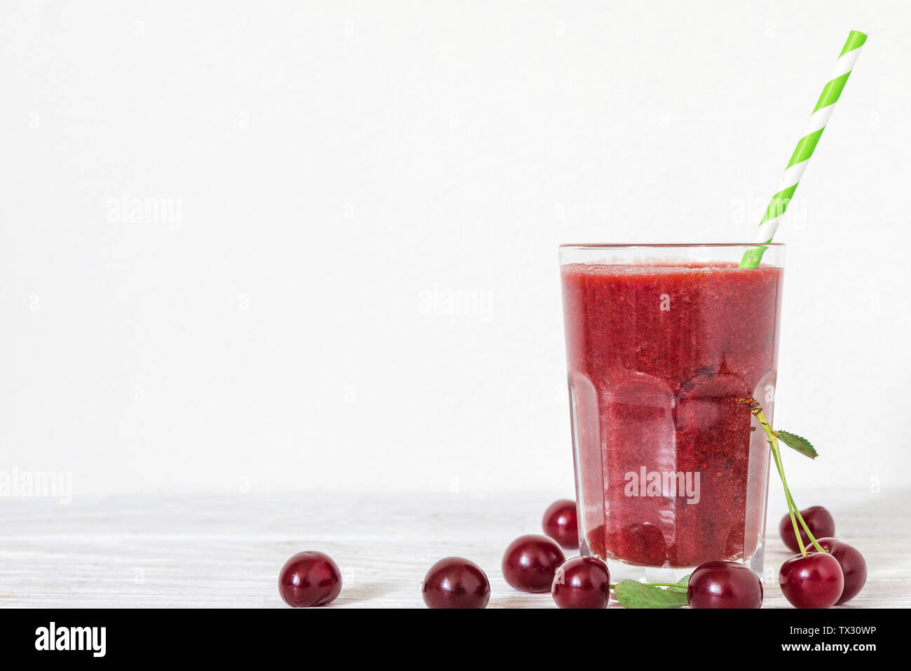 Frullato di ciliegia in un bicchiere con una cannuccia e frutti di bosco freschi su sfondo bianco con copia spazio. bevanda estiva. una sana dieta vegana Foto Stock