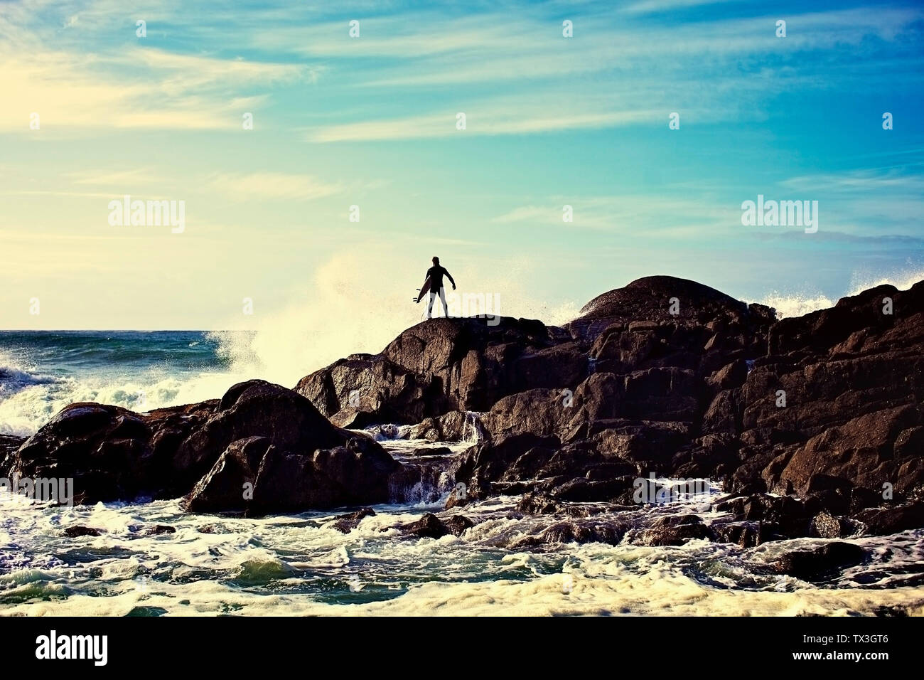 Silhouette surfista maschio guarda l'oceano onde infrangersi contro le rocce di sunny beach, Tofino, Canada Foto Stock