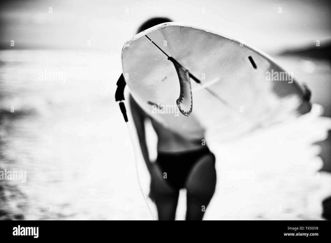 Surfista femmina che trasportano le tavole da surf sulla spiaggia dell'oceano Foto Stock