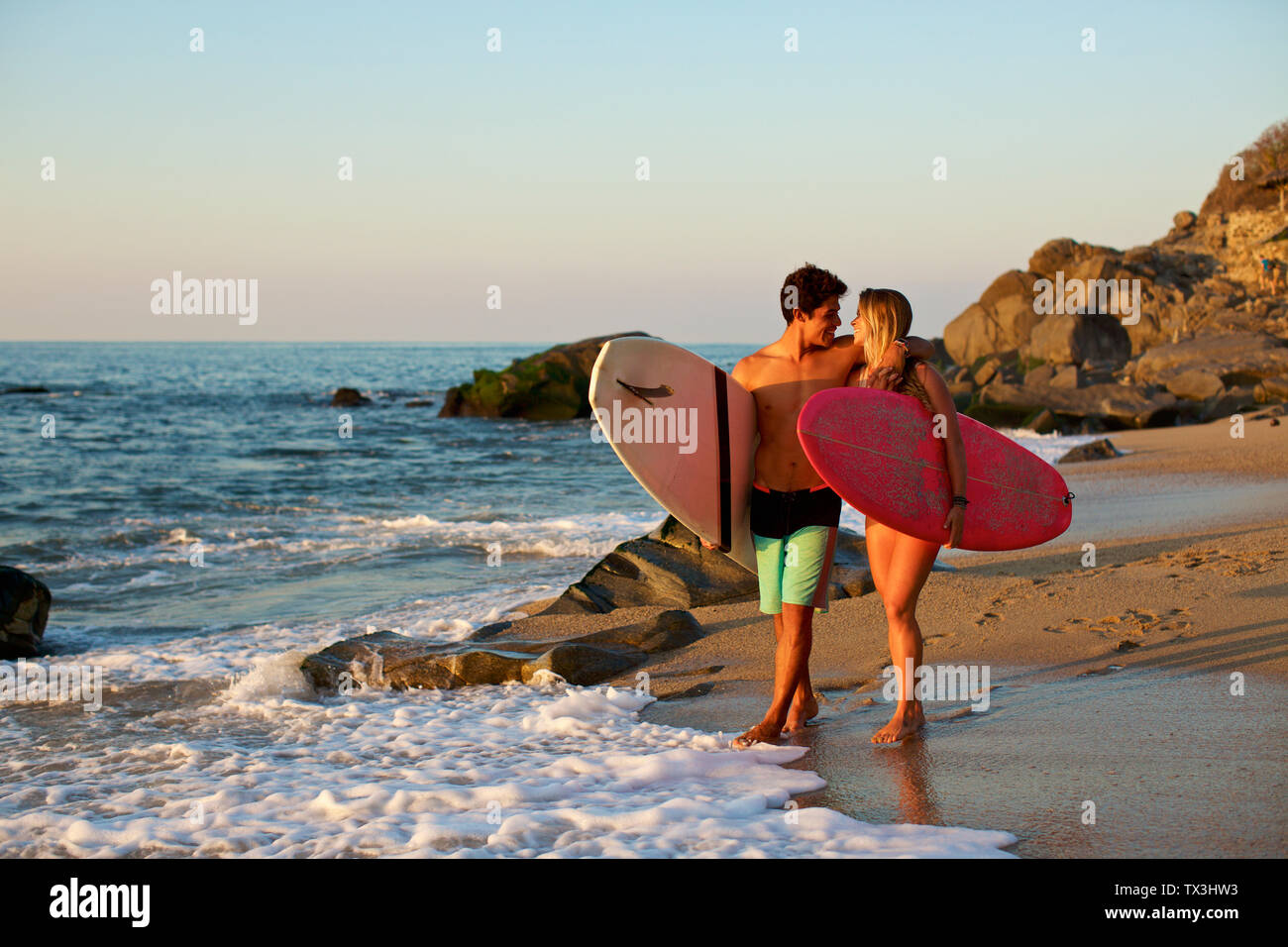 Giovani, affettuosa giovane con tavole da surf camminando sulla soleggiata spiaggia oceano, Sayulita, Nayarit, Messico Foto Stock