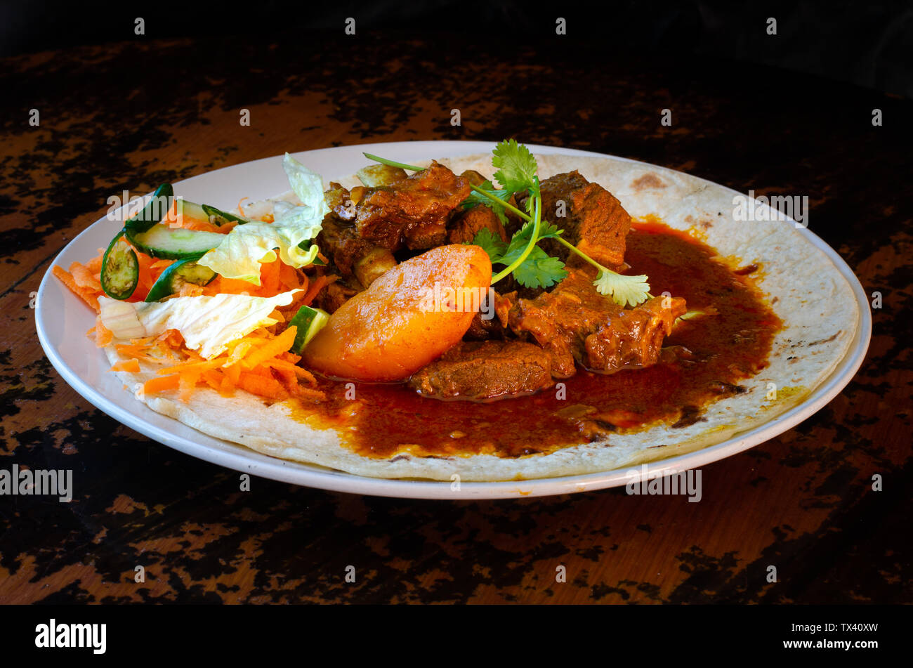 Un curry di montone roti con sambals - un iconico Durban pasto composto da un roti condito con curry di montone e sugo di carne. Il sambals sono carote grattugiate con c Foto Stock