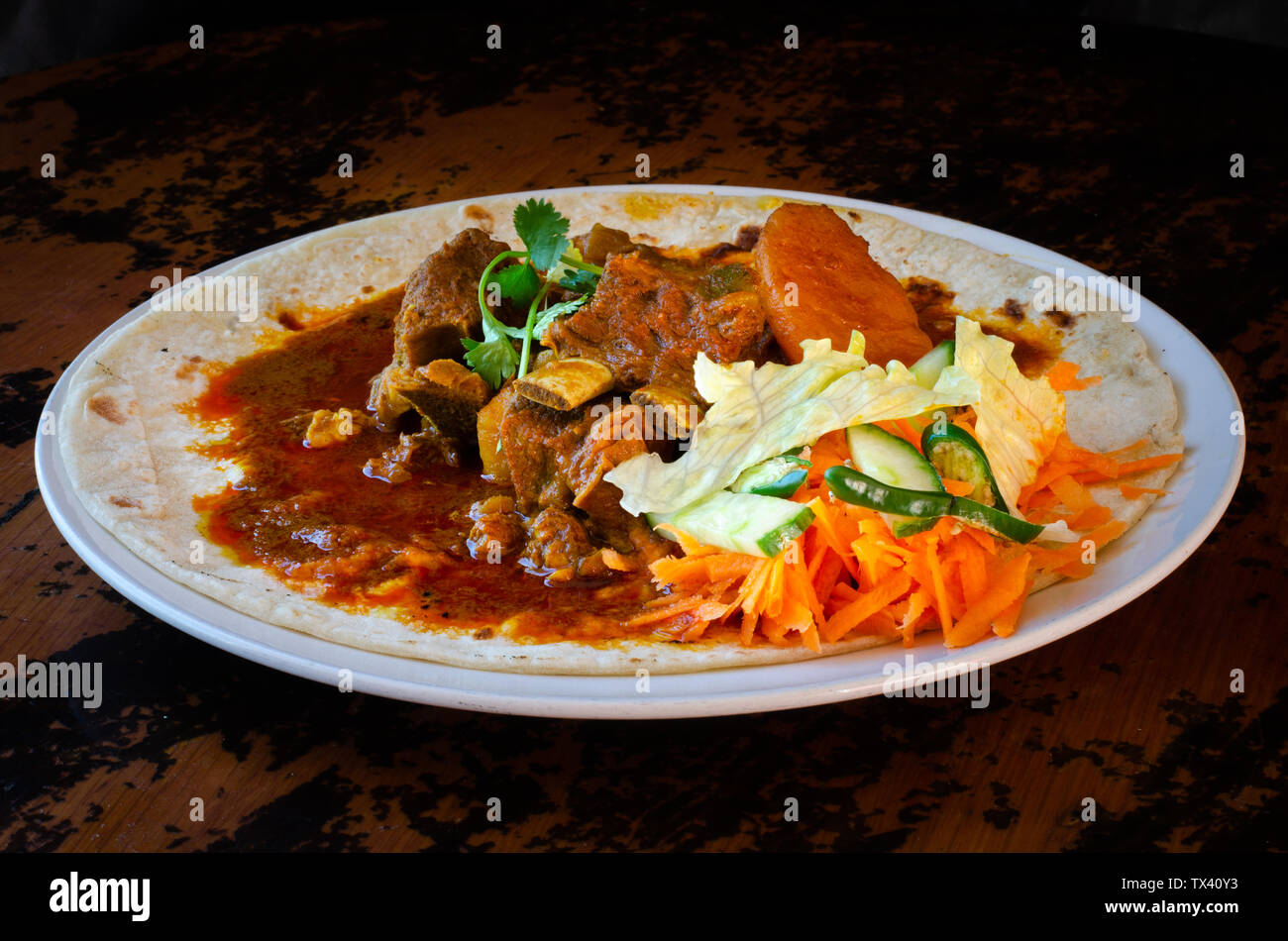 Un curry di montone roti con sambals - un iconico Durban pasto composto da un roti condito con curry di montone e sugo di carne. Il sambals sono carote grattugiate con c Foto Stock