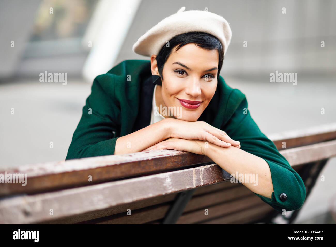 Ritratto di sorridere di moda giovane donna seduta su una panchina Foto Stock