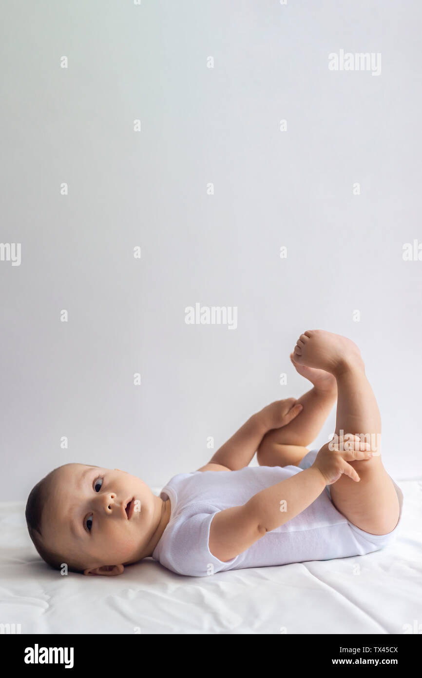 6-mese baby divertendosi in biancheria da letto bianca. Carino il bambino giacente sul letto. Famiglia, vita nuova concezione dell'infanzia. Foto Stock