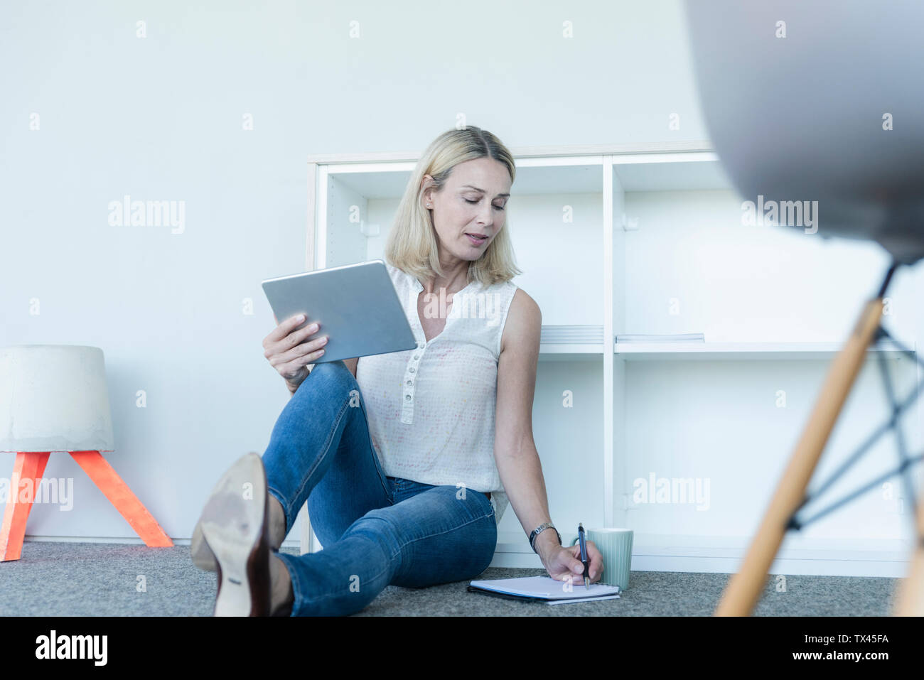 Casual imprenditrice seduta sul pavimento in ufficio utilizzando tablet e prendere note Foto Stock