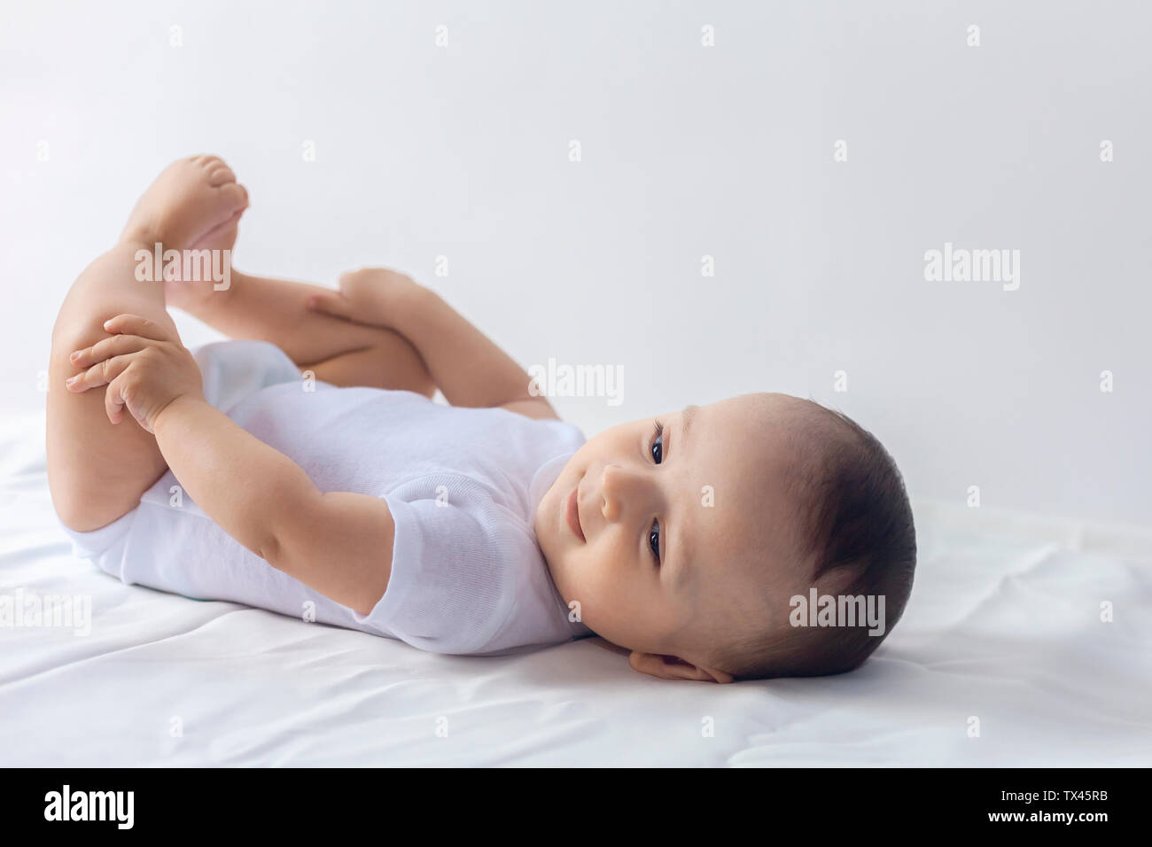 6-mese baby divertendosi in biancheria da letto bianca. Carino il bambino giacente sul letto. Famiglia, vita nuova concezione dell'infanzia. Foto Stock