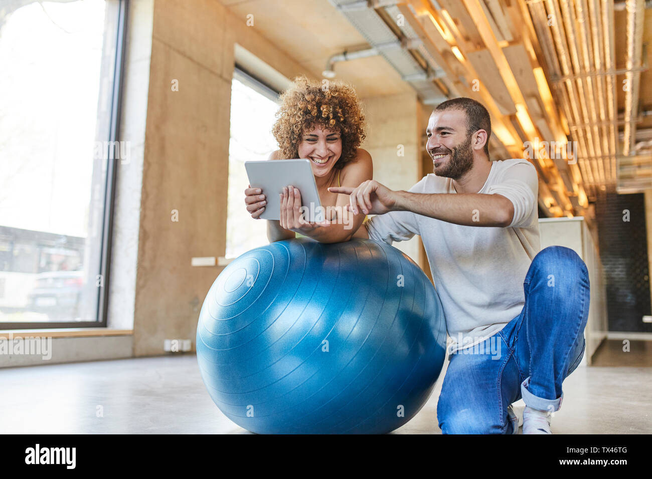 Felice l'uomo e la donna utilizzando compressa sulla sfera di fitness in ufficio moderno Foto Stock