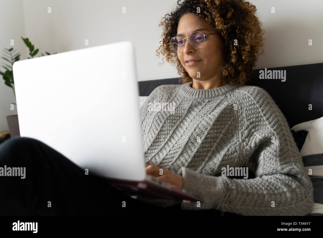Donna seduta sul letto, utilizzando laptop, navigando in rete Foto Stock