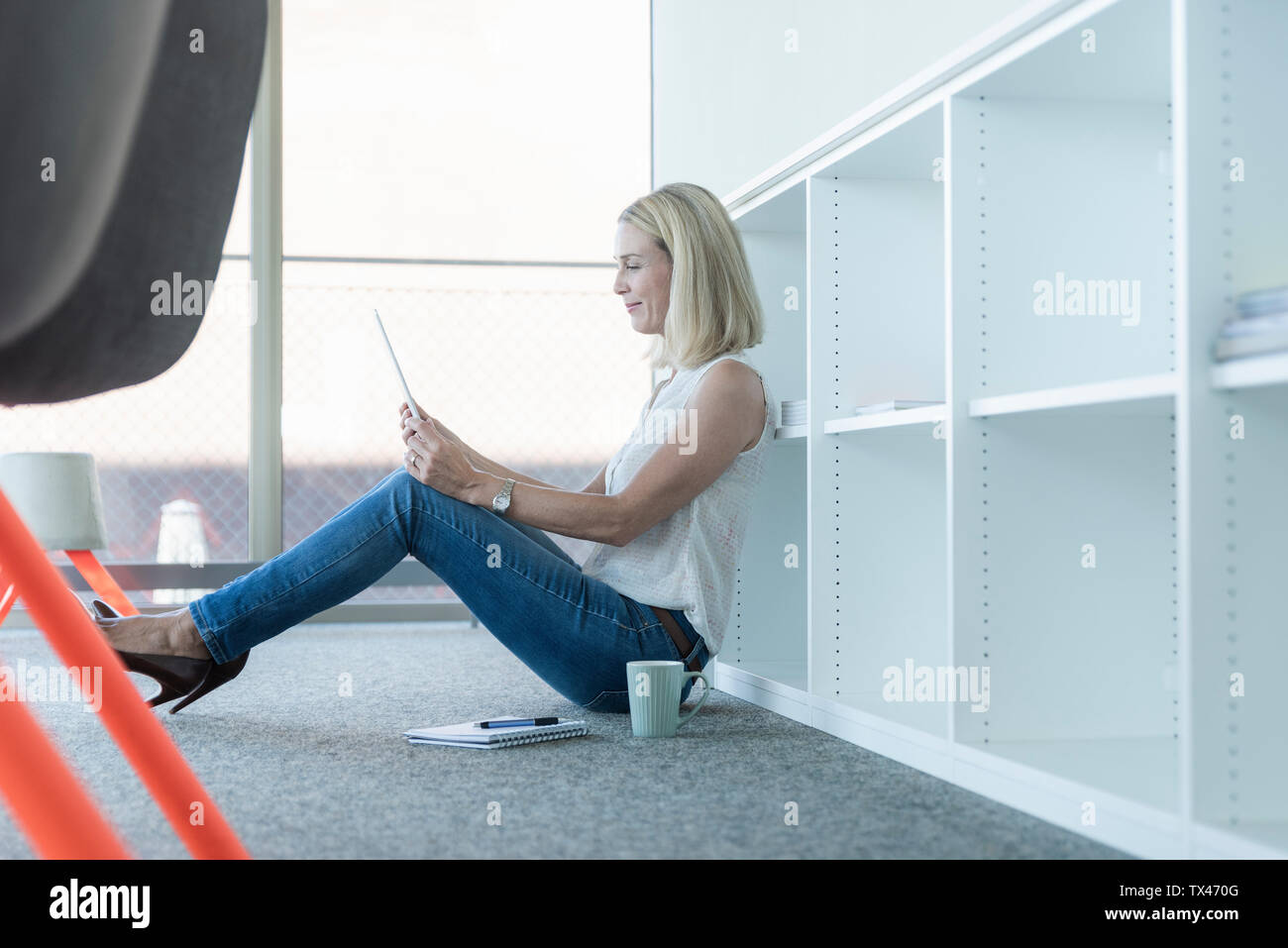 Casual imprenditrice seduta sul pavimento in ufficio utilizzando tablet Foto Stock