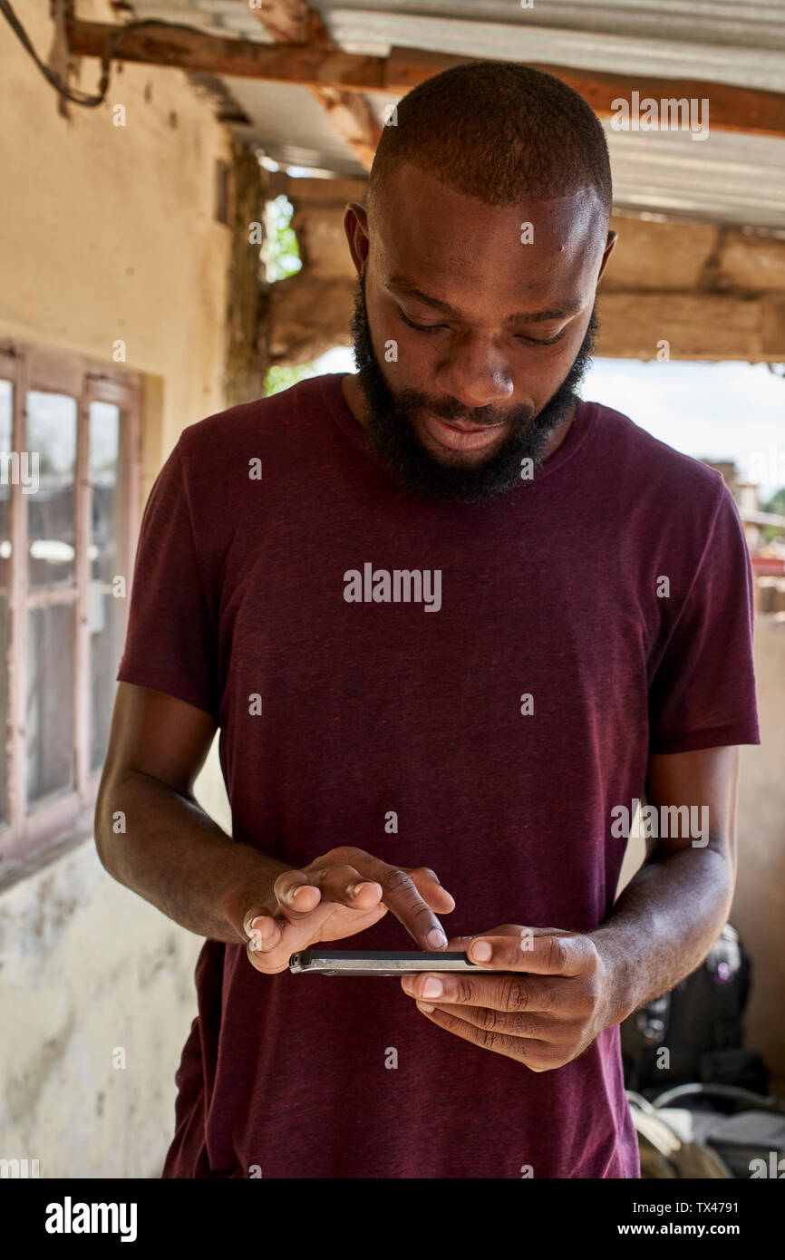 Mozambico Maputo, giovane uomo sulla veranda utilizza lo smartphone Foto Stock