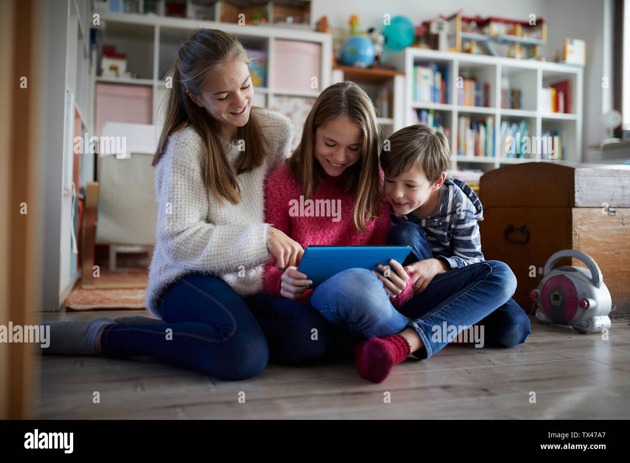 I fratelli a giocare a casa con loro compresse digitale, seduti a terra Foto Stock