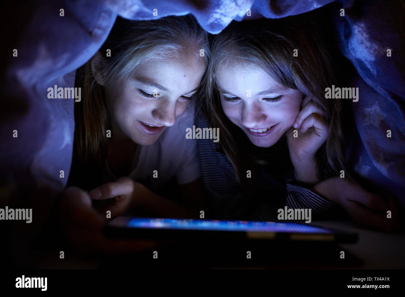 Due sorelle giocando segretamente con la loro tavoletta digitale, nascosto sotto la coperta Foto Stock