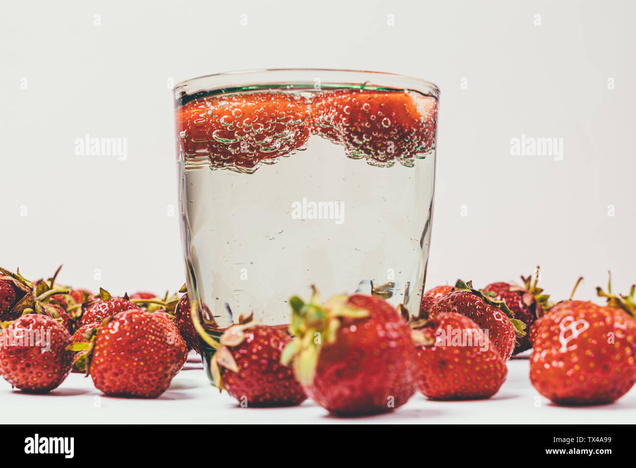 Close-up di bicchiere di acqua frizzante con bolle e fragole accanto ai frutti di bosco freschi su sfondo bianco. Foto Stock