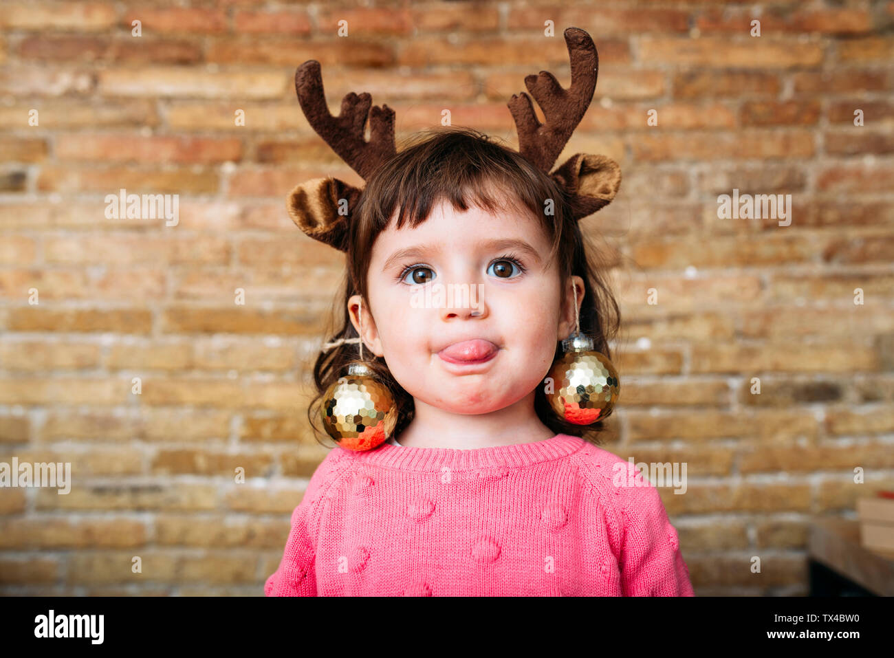 Ritratto di ragazza toddler spuntavano lingua indossando le renne palchi archetto e baubles di Natale Foto Stock
