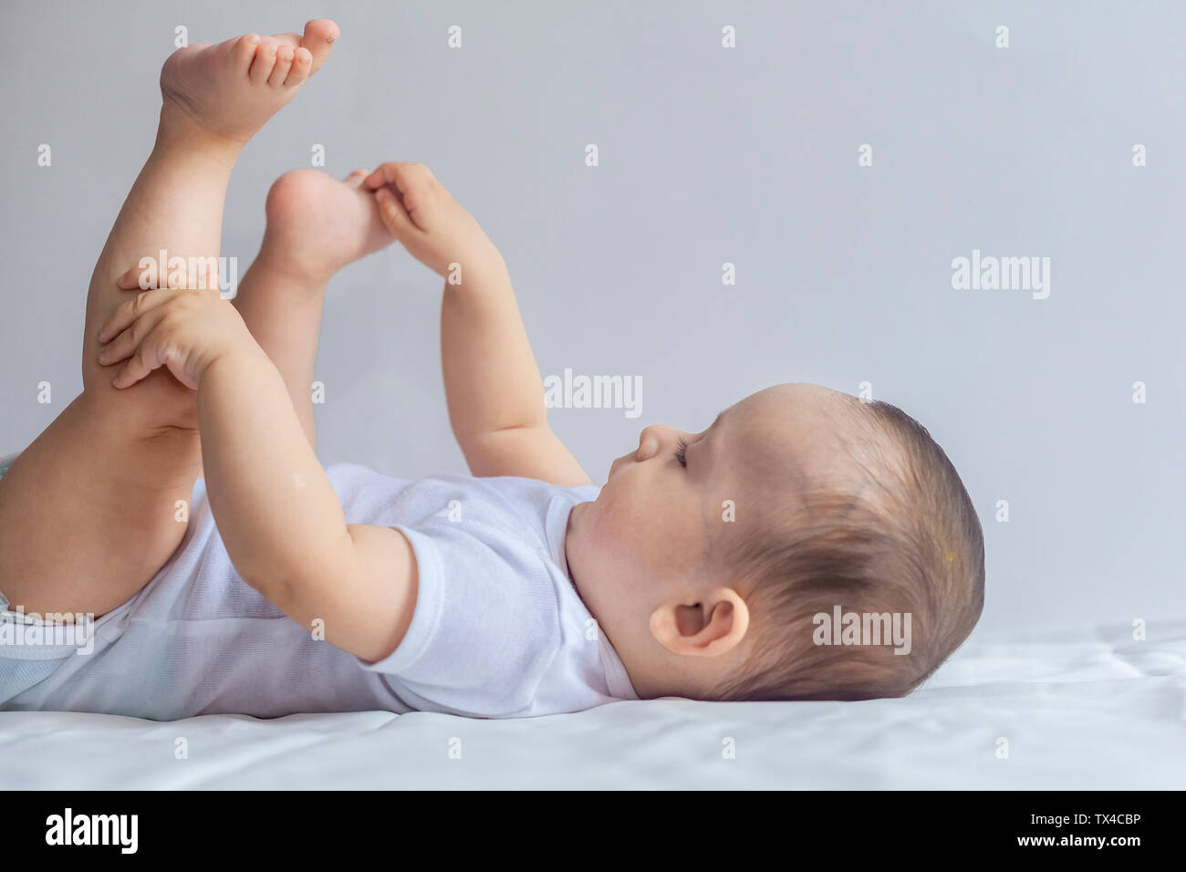 6-mese baby divertendosi in biancheria da letto bianca. Carino il bambino giacente sul letto. Famiglia, vita nuova concezione dell'infanzia. Foto Stock