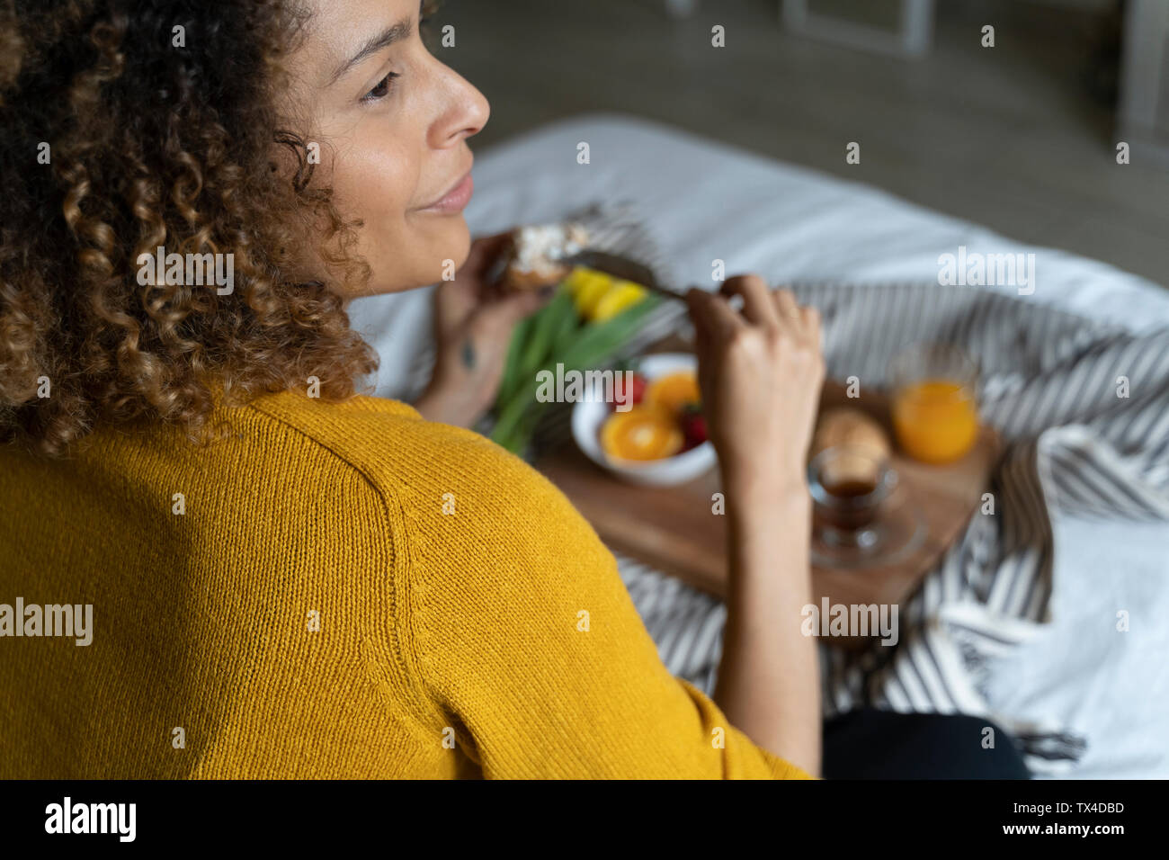 Donna seduta sul letto, avente una sana prima colazione Foto Stock