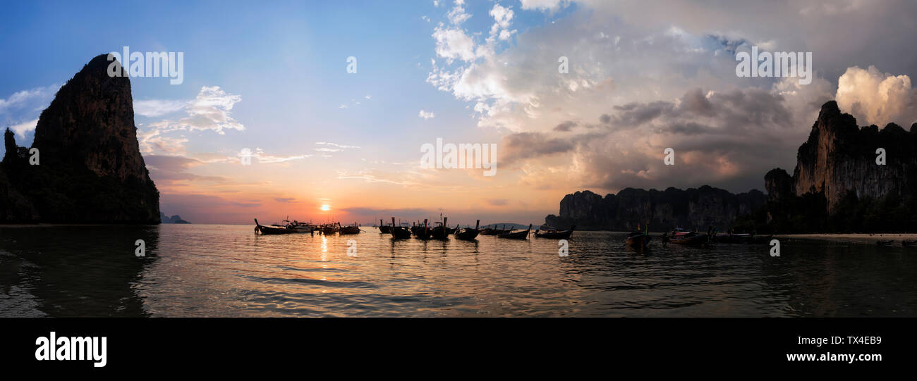 Thailandia, Krabi, Railay Beach, baia con coda lunga barche galleggiante sull'acqua al tramonto Foto Stock