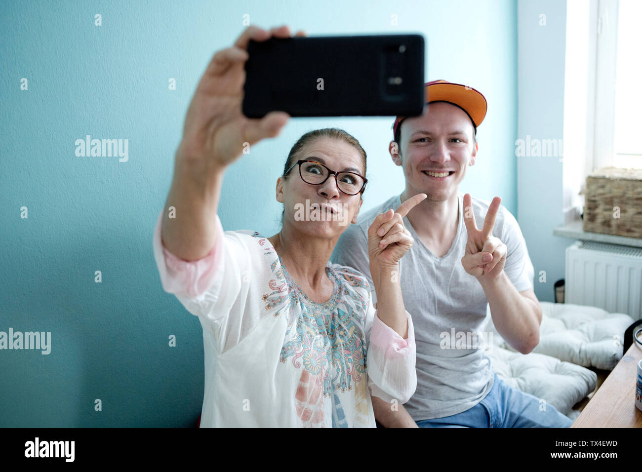La madre e il Figlio seduto al tavolo della cucina, tenendo smarrtphone selfies Foto Stock
