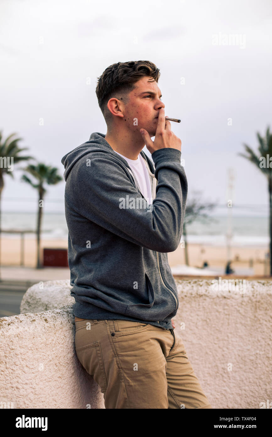 Giovane uomo di fumare un giunto con palme in background Foto Stock