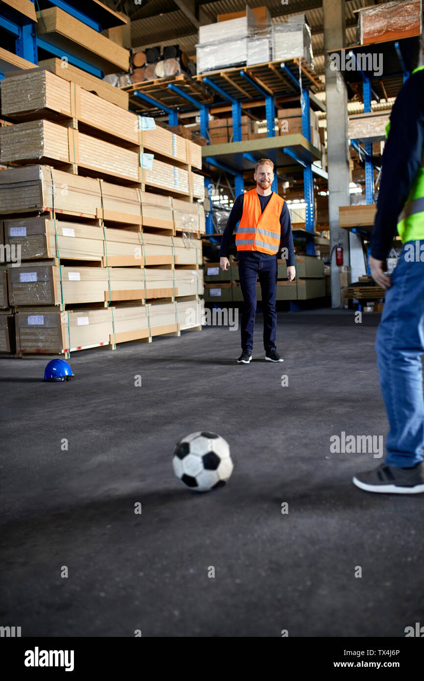 Lavoratori a giocare a calcio nel magazzino di fabbrica Foto Stock