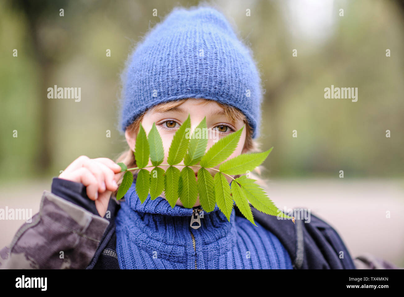 Ritratto ragazzo indossa blue hat e maglione guardando attraverso la foglia verde Foto Stock
