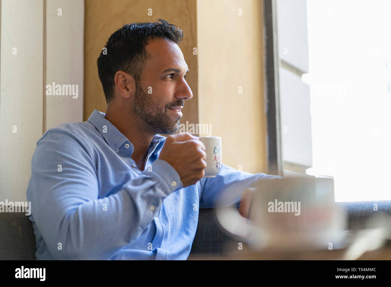 Imprenditore sorridente con tazza di caffè guardando fuori della finestra Foto Stock