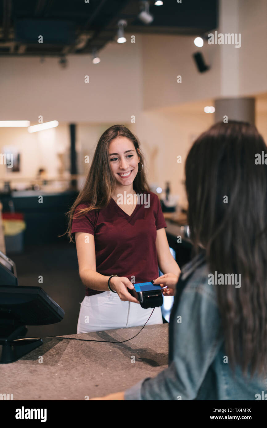 Giovane donna di pagare senza contanti con carta di credito presso il bancone di un bar Foto Stock