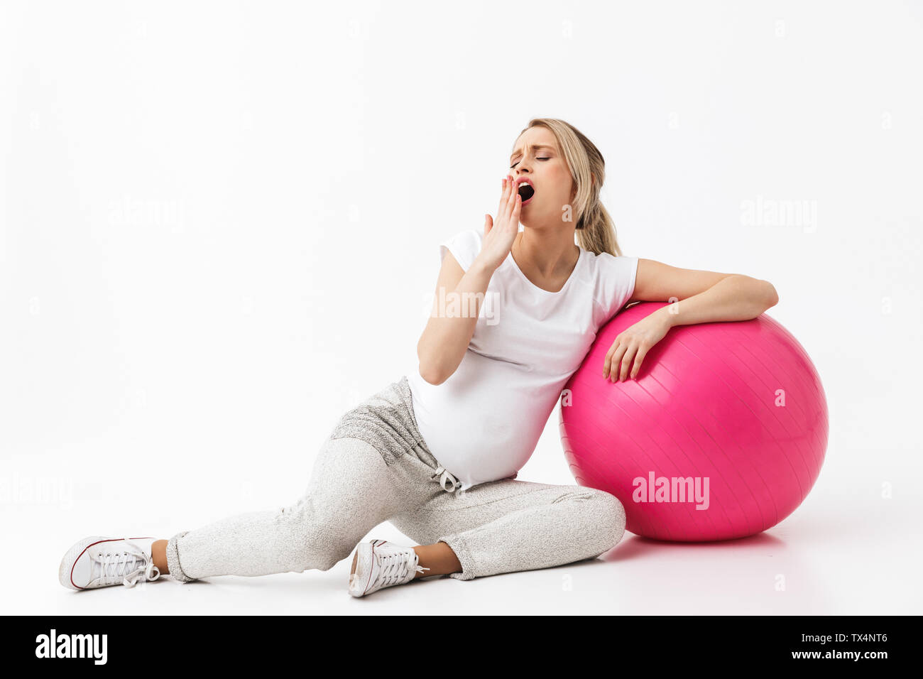 Immagine di una bella sbadigli giovani incinte fitness yoga donna posa isolate su muro bianco sullo sfondo si trova sulla sfera. Foto Stock