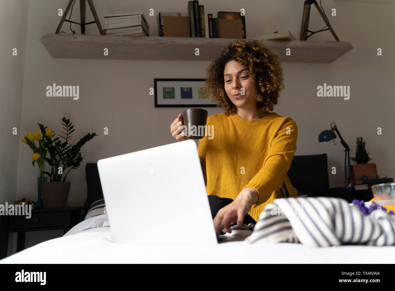 Donna seduta sul letto, utilizzando laptop, bere caffè Foto Stock
