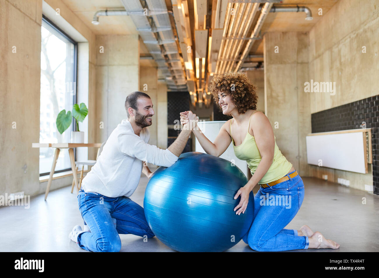 Felice l'uomo e donna wrestling braccio sulla sfera di fitness in ufficio moderno Foto Stock