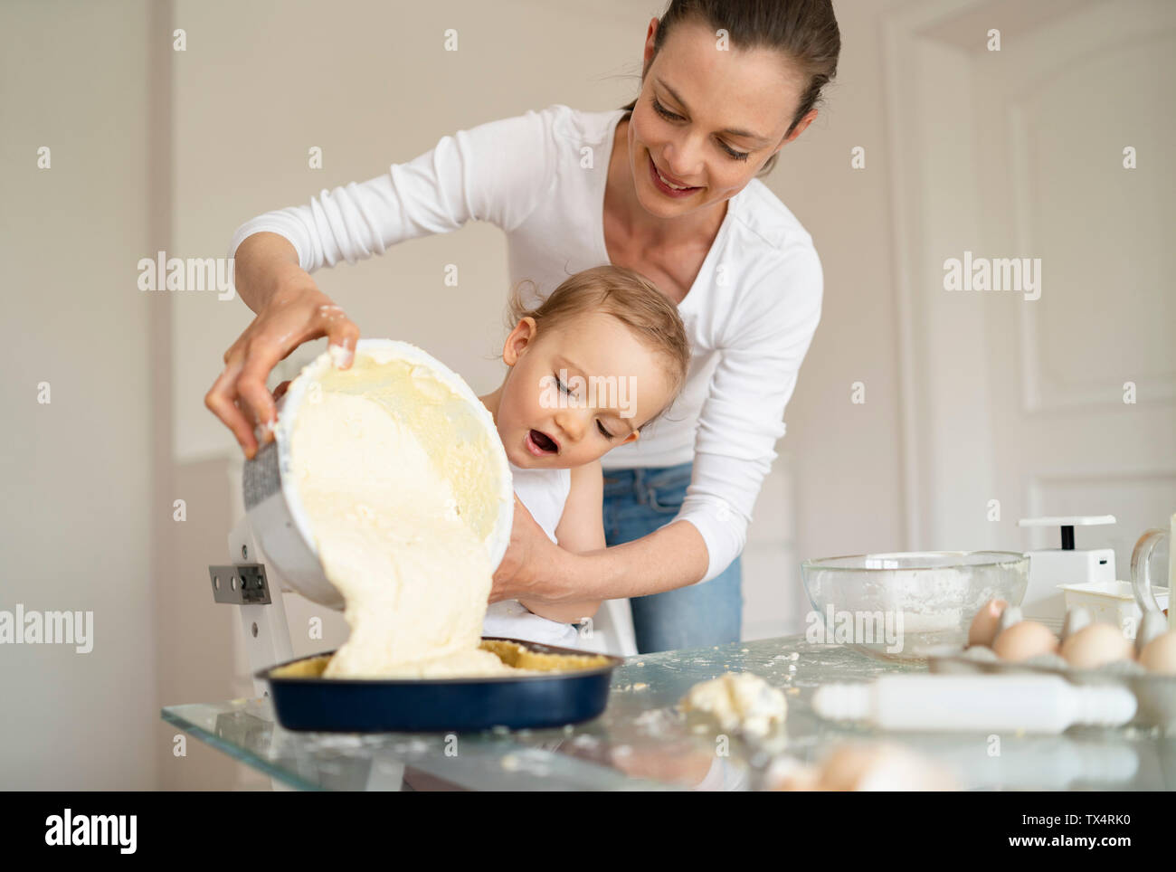 Madre e figlia piccola realizzazione della torta insieme versando l'impasto nella teglia da forno Foto Stock