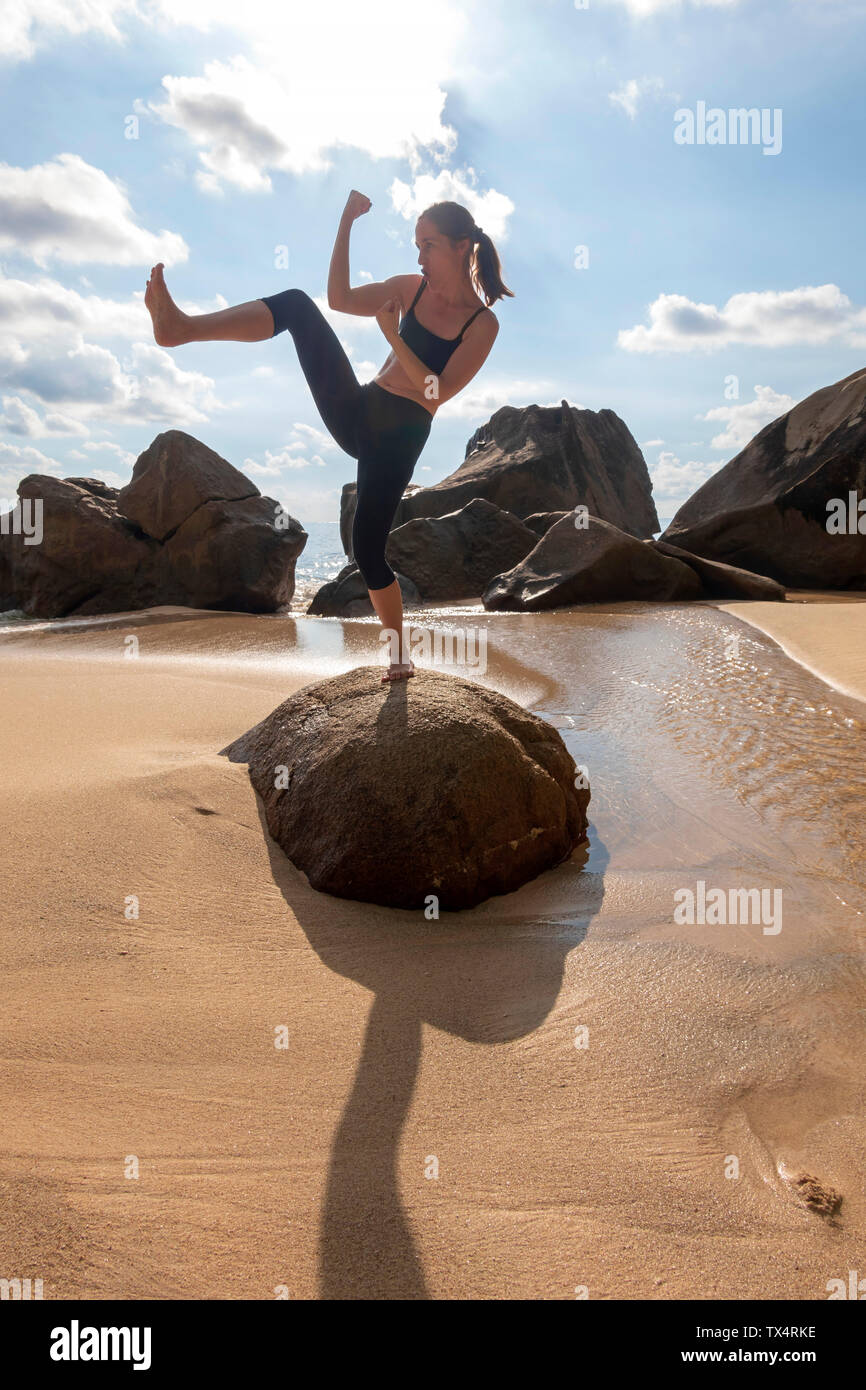 Seychelles, Mahe, Takamaka Beach, donna in piedi su una roccia shadowboxing Foto Stock