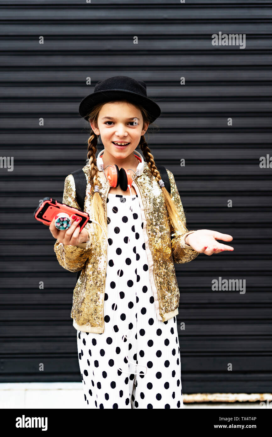 Ritratto di ragazza sorridente con lo smartphone indossando hat, golden sequin jacket e polka dot tuta Foto Stock