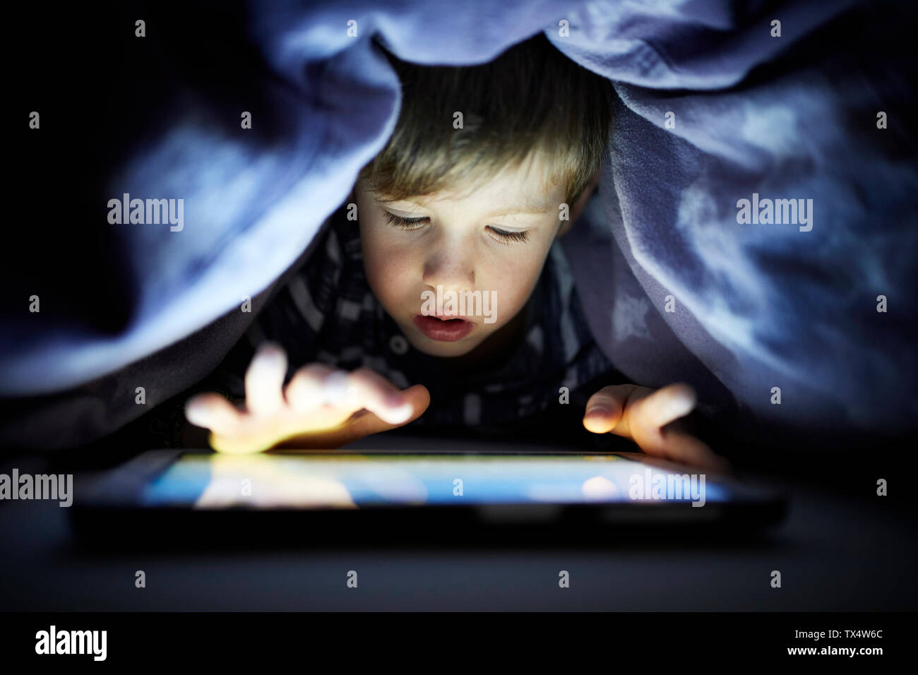 Little Boy giocando segretamente con la sua tavoletta digitale, nascosto uunder coperta Foto Stock