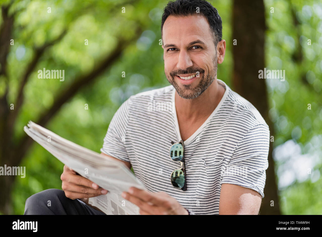 Ritratto di uomo sorridente leggendo il giornale in park Foto Stock