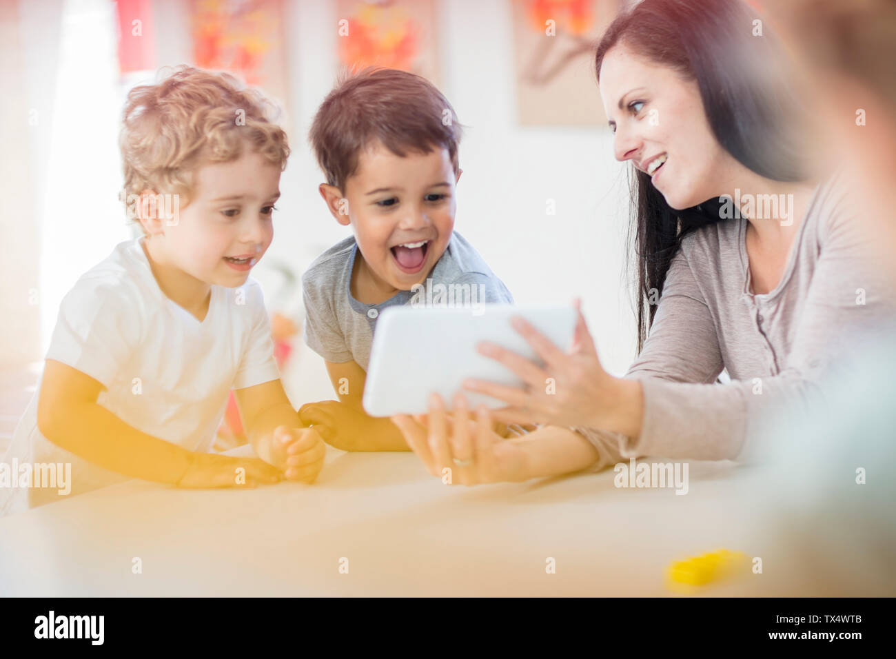 Pre-insegnante della scuola mostrando mini tablet a felice ragazzi nella scuola materna Foto Stock