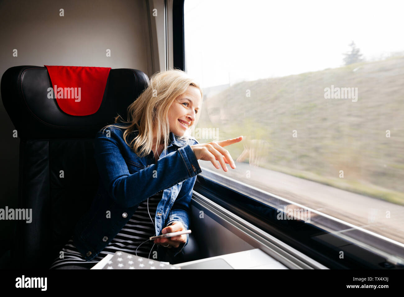 Sorridente donna bionda che viaggiano in treno guardando fuori della finestra Foto Stock