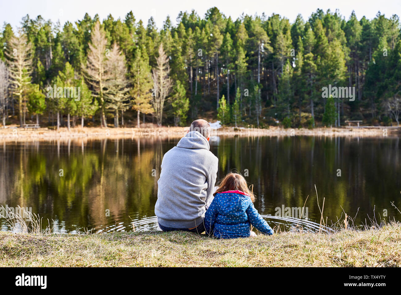 Francia, Pirenei, vista posteriore del padre e figlia piccola seduta a fianco a fianco di fronte ad un lago Foto Stock
