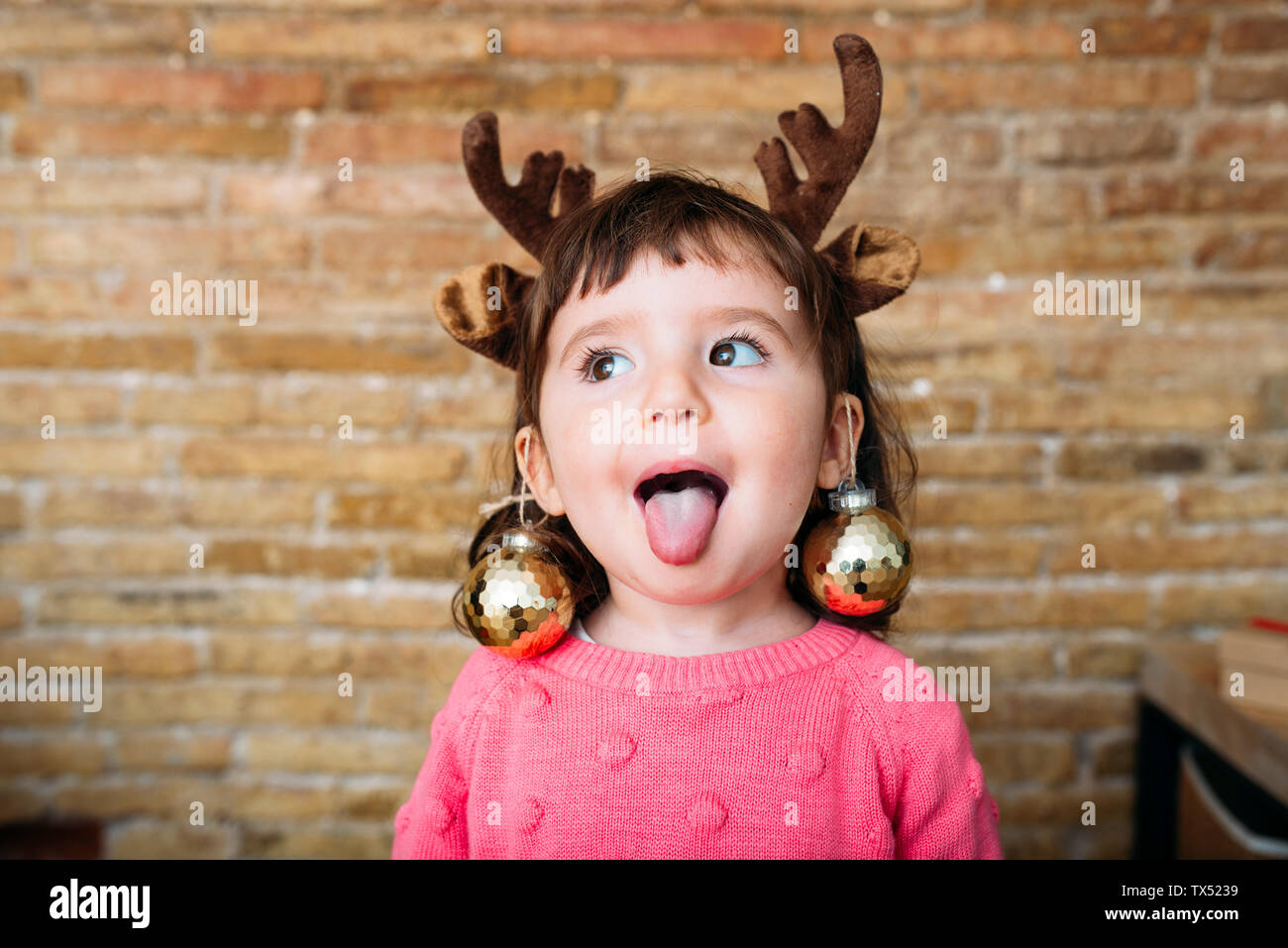 Ritratto di ragazza toddler spuntavano lingua indossando le renne palchi archetto e baubles di Natale Foto Stock