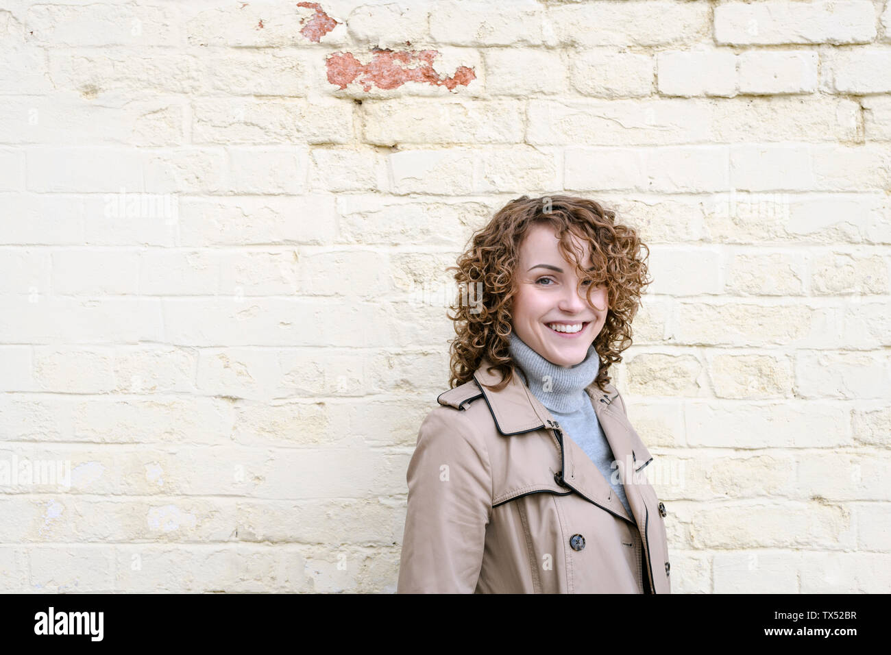 Ritratto di donna felice con i capelli ricci di fronte a un muro di mattoni Foto Stock